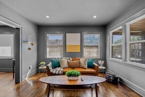 A modern living room with a brown leather sofa, a round wooden coffee table, and a view through large windows. - #28- *Modern Bungalow* (New Britain)