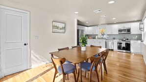 Una cocina moderna con armarios blancos, un comedor con mesa de madera y sillas azules, y una puerta blanca.