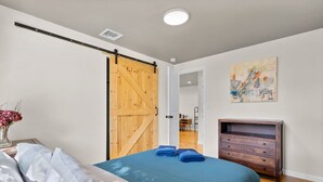 Un dormitorio con una cama, un aparador de madera, una puerta corrediza tipo granero y un cuadro en la pared.