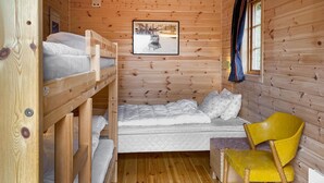 Une pièce de cabane en bois avec des lits superposés, un lit simple, une chaise jaune et un tableau encadré au mur.
