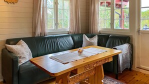 Un canapé en cuir vert, une table en bois devant, deux fenêtres avec des rideaux et une horloge au mur.