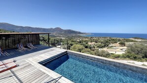 A pool with a wooden deck and lounge chairs, overlooking a coastal landscape with mountains and a clear sky. - Villa Casa di C (Corbara)