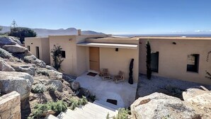 A modern building with a flat roof, large rocks, and a clear view of the mountains in the background. - Villa Casa di C (Corbara)