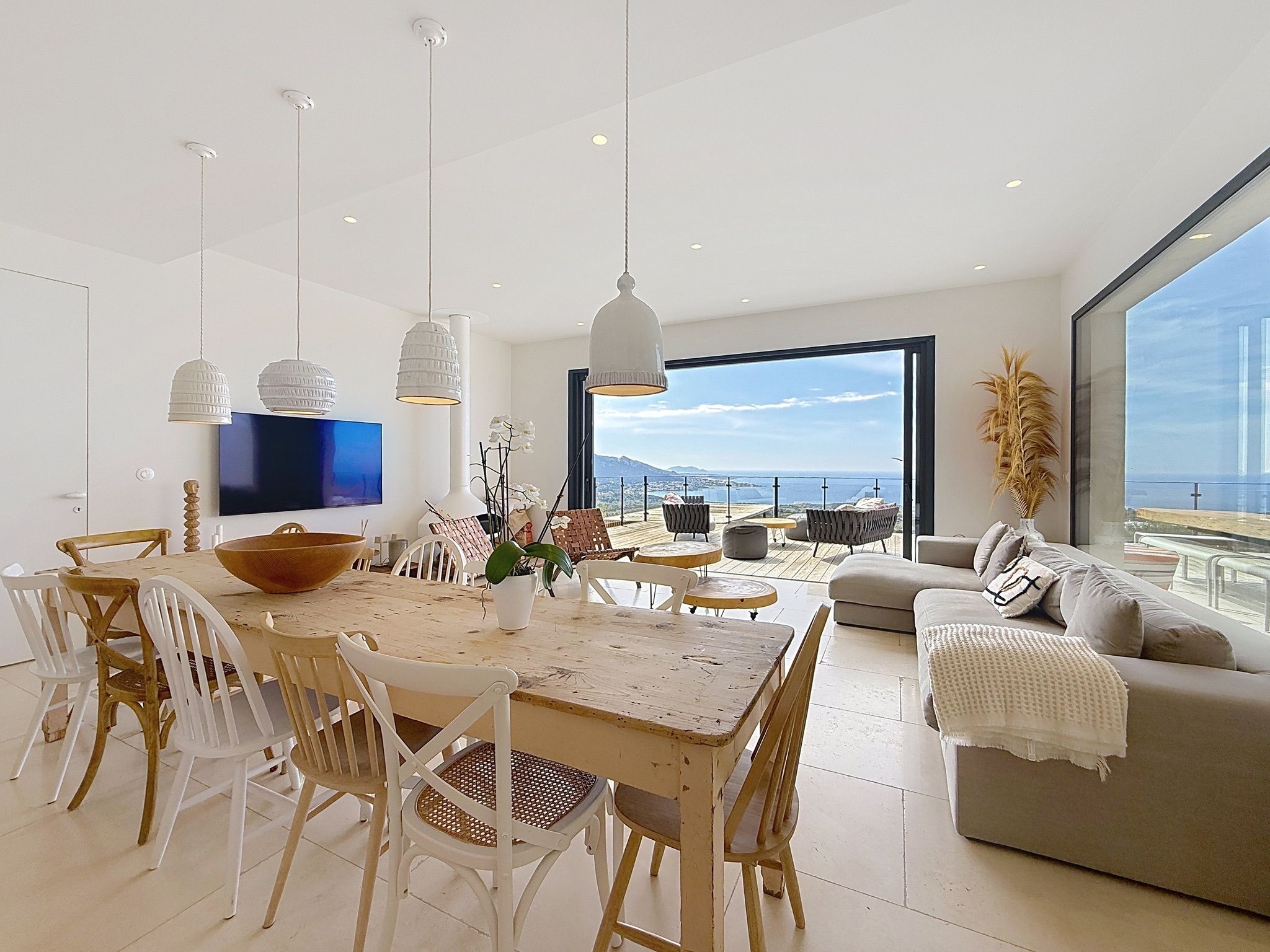 A modern living room with a dining area, large windows, and a flat-screen TV.