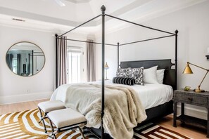 Ein Bett mit Baldachin, eine fellüberwurf, ein runder Spiegel und ein Nachttisch mit Lampe.