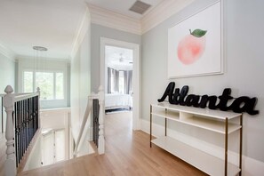 A staircase with a white railing, a white console table with gold legs, and a wall-mounted sign that reads "Atlanta". - Carmelot (Atlanta)