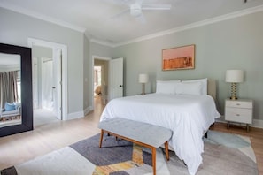 Un dormitorio con una cama grande, mesitas de noche, un banco y un ventilador de techo.