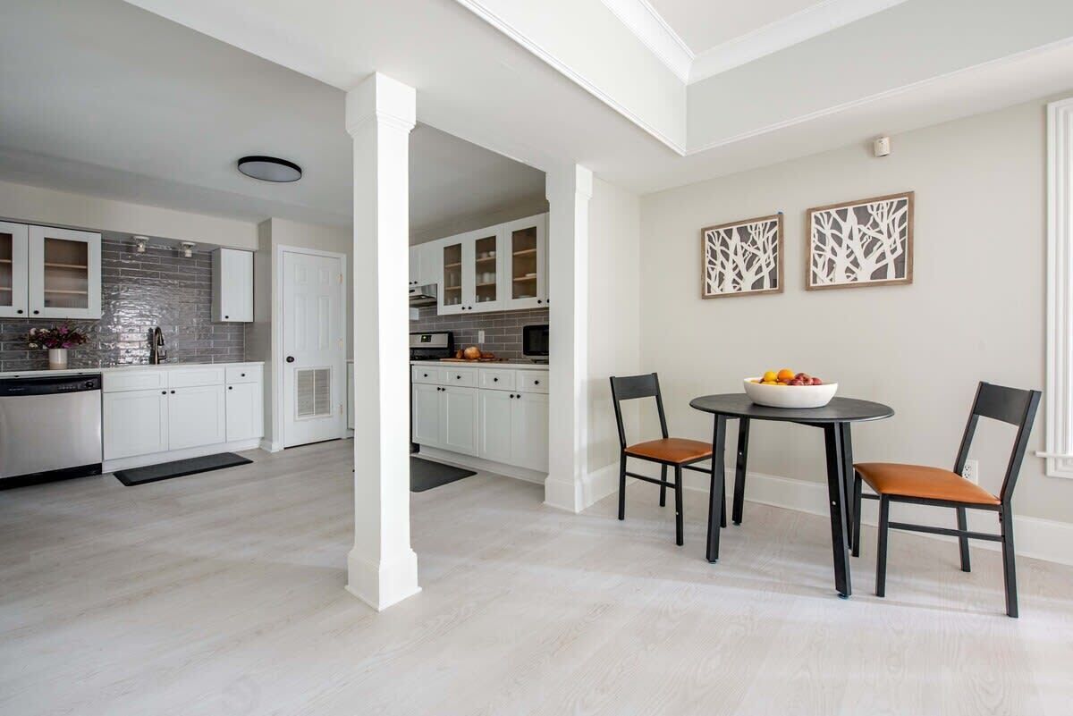 Een moderne keuken met witte kastjes, een zwart aanrecht en een eethoek met twee stoelen en een tafel.