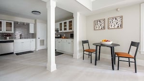 A modern kitchen with white cabinets, a black countertop, and a dining area with two chairs and a table.
