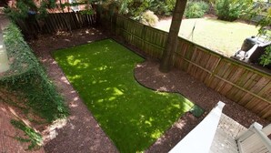 A backyard with a fenced area, a tree, and a grill.