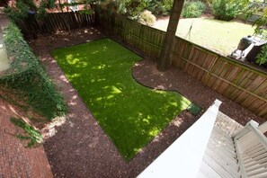 Un patio trasero con área cercada, un árbol y una parrilla.