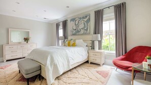 A bedroom with a bed, bedside tables, a chair, a dresser, a mirror, and a window with curtains. - Creme Carmel (Atlanta)