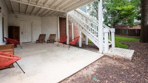A covered patio with a white railing, red chairs, and a brick wall. - Creme Carmel (Atlanta)