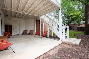 A covered patio with a white railing, red chairs, and a brick wall.
