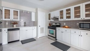 A modern kitchen with white cabinets, a dishwasher, an oven, and a microwave.