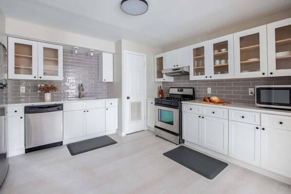 A modern kitchen with white cabinets, a dishwasher, an oven, and a microwave.