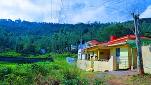 A house with a red roof, surrounded by lush greenery and hills. - Rena Home Stay (Yercaud)