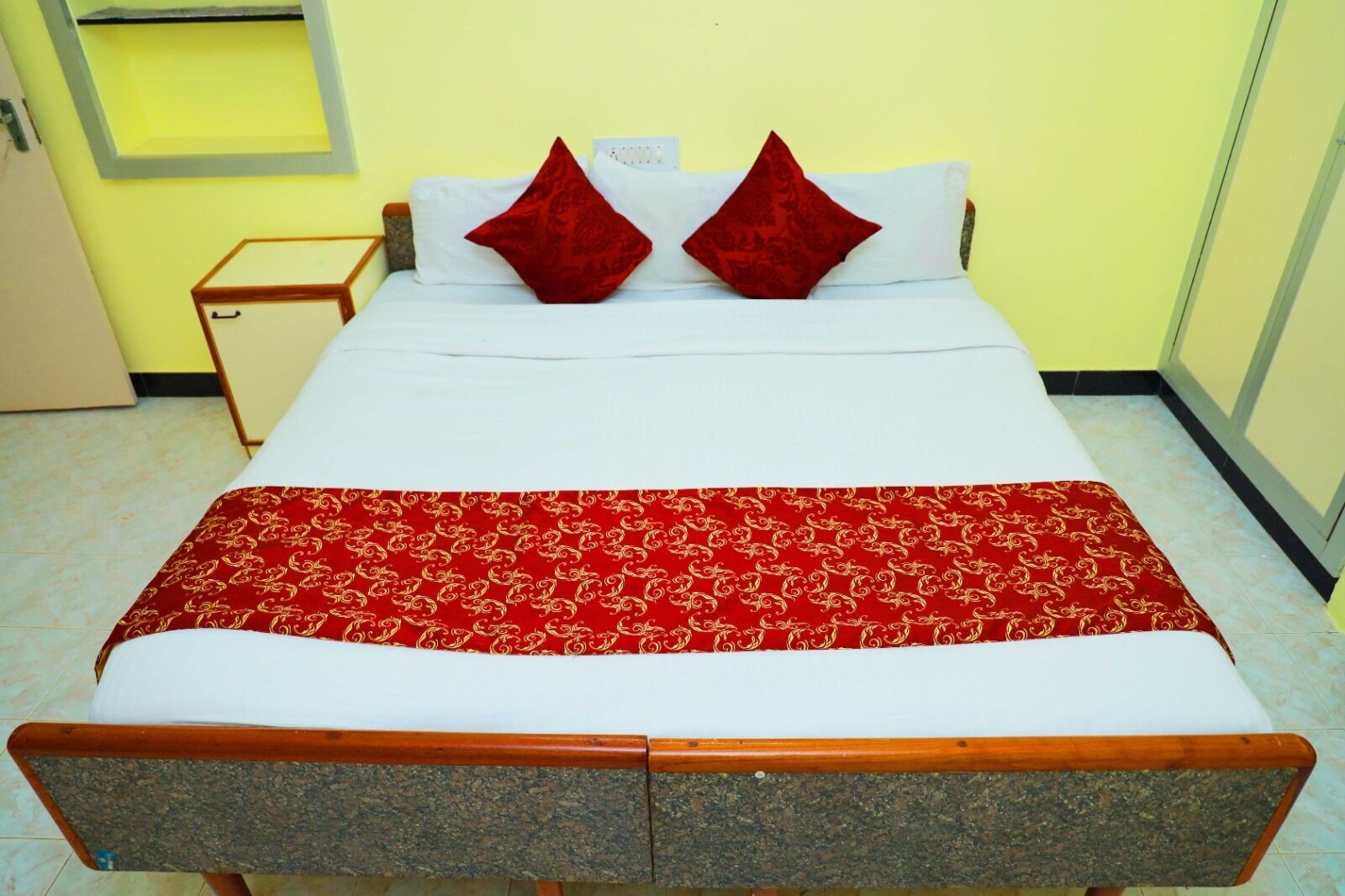Un lit avec une couvre-lit à motifs rouges, deux oreillers rouges et une tête de lit en bois.