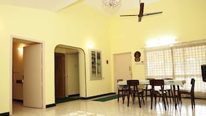 A dining area with a table and chairs, a ceiling fan, and a window with curtains. - Rena Home Stay (Yercaud)