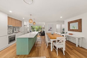 Eine moderne Küche mit einer zentralen Kochinsel, weißen Schränken und einem Essbereich mit einem Holztisch und weißen Stühlen.