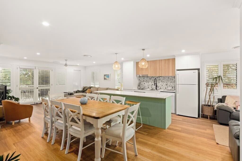 A modern kitchen with a central island, white cabinetry, and a dining area with a wooden table and white chairs.