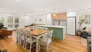 Une cuisine moderne dotée d’un îlot central, de meubles blancs et d’un coin repas avec une table en bois et des chaises blanches.