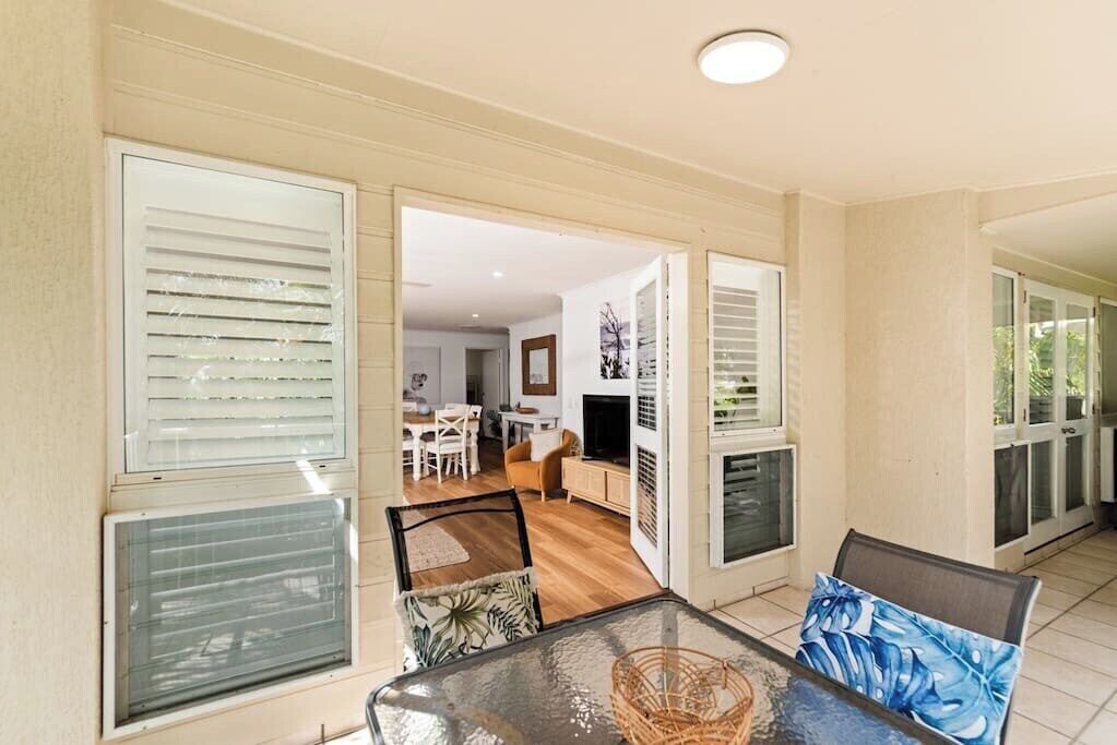 A spacious room with a glass table, a wicker chair, and a sofa with a blue cushion.