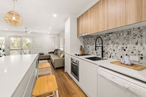 Une cuisine moderne avec des meubles blancs, un grand îlot central et un pare-feu au motif moucheté.