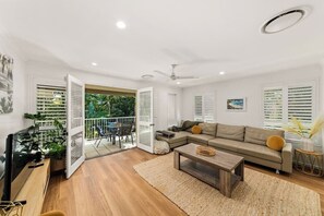 Ein modernes Wohnzimmer mit einer Couch, einem Couchtisch und einem Fernseher. Ein Balkon bietet Blick auf Grünflächen.