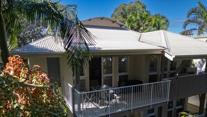 Un immeuble à plusieurs étages doté de balcons, d’un espace extérieur aménagé pour s’asseoir et d’une végétation tropicale.