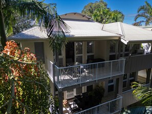 A multi-story building with balconies, outdoor seating, and tropical vegetation.