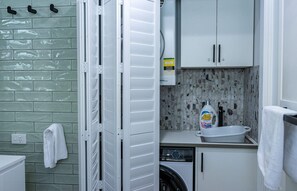 Une petite buanderie équipée d’un lave-linge, d’un évier et de placards.