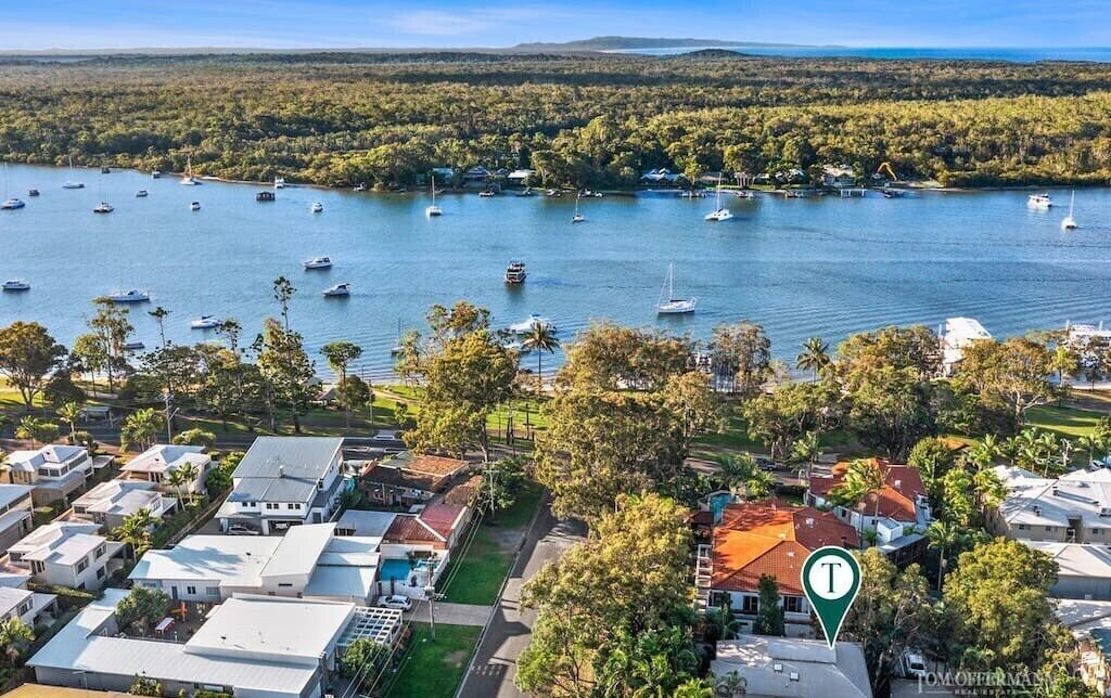 An aerial view of a coastal residential area with houses, a marina with boats, and a prominent 'T' marker.