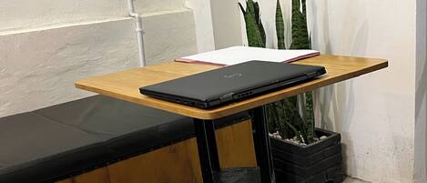 A wooden desk with a laptop, a notebook, and a potted plant.