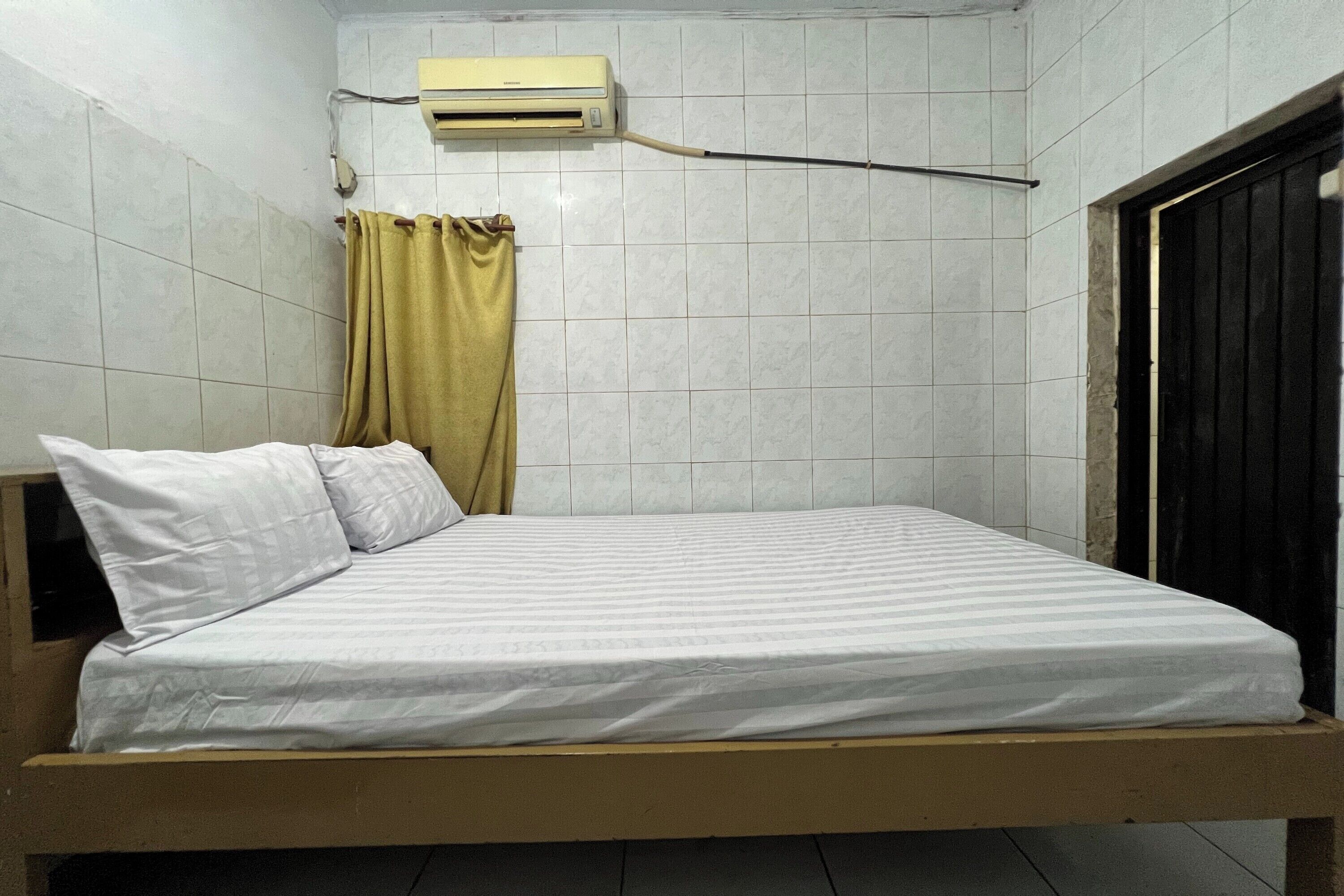 A single bed with white bedding in a room with tiled walls, a curtain, and an air conditioning unit.