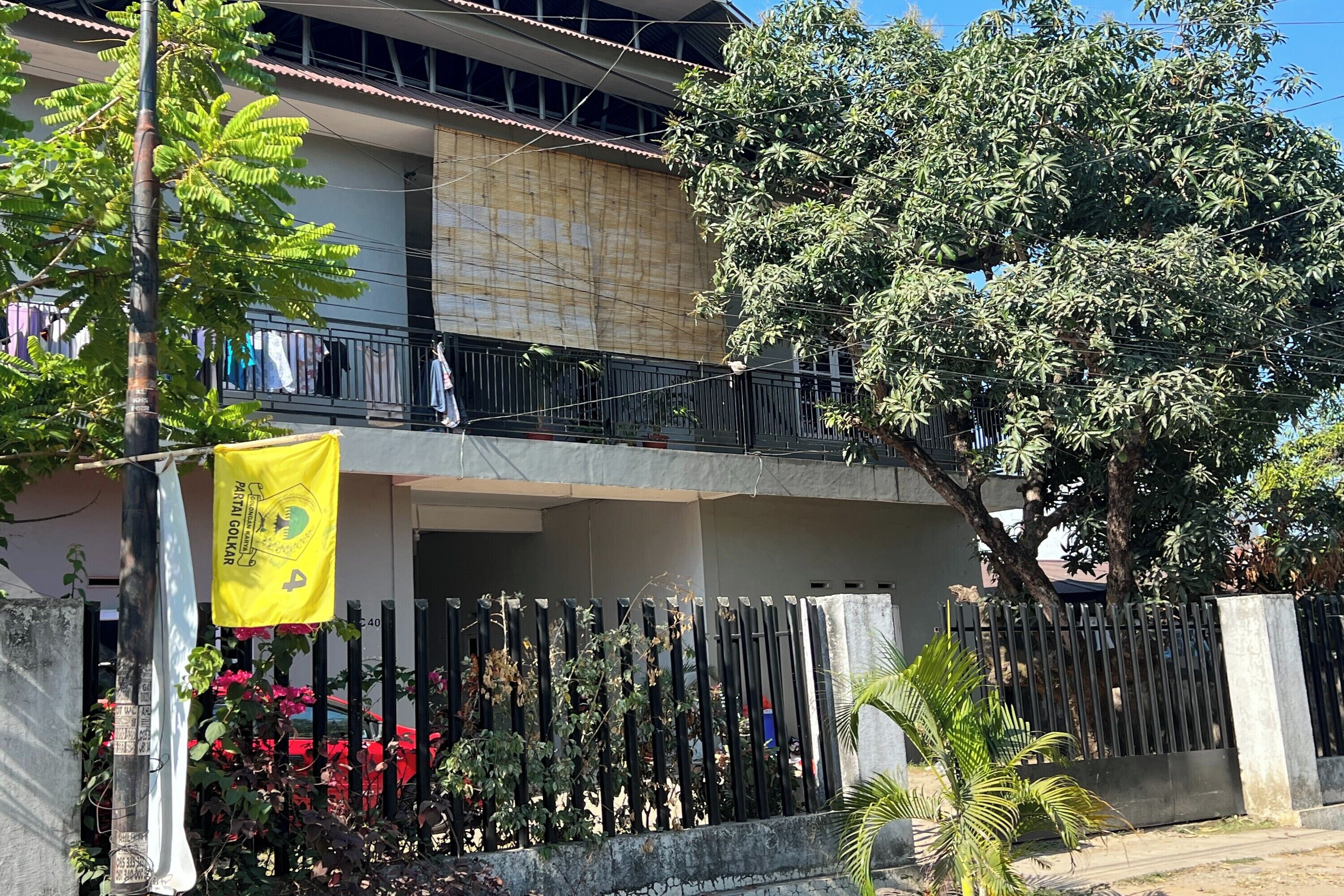 Un bâtiment à deux étages doté d’un balcon, entouré d’arbres et d’une clôture.