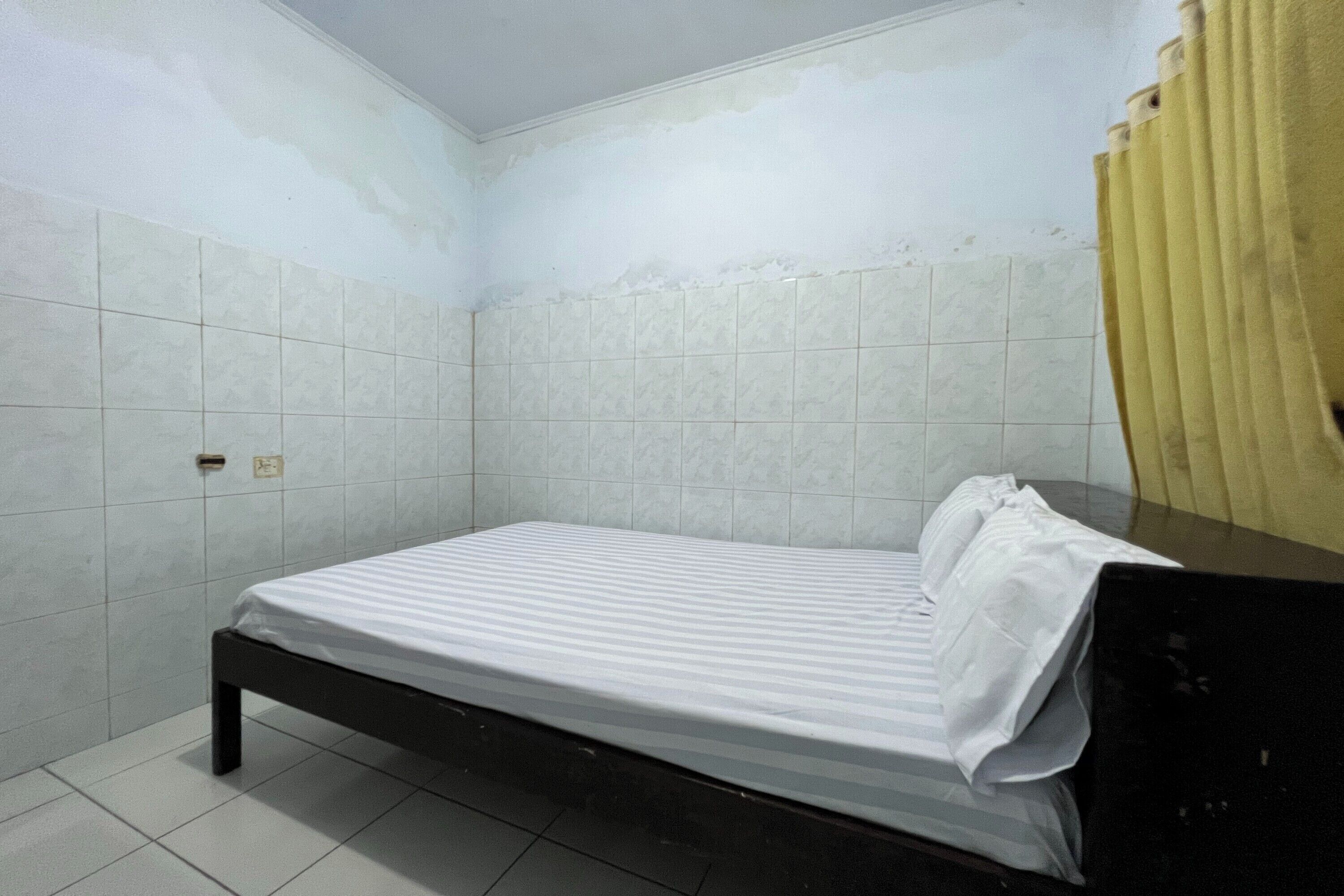 Une petite chambre avec un lit simple, des murs carrelés de blanc et une tête de lit noire.