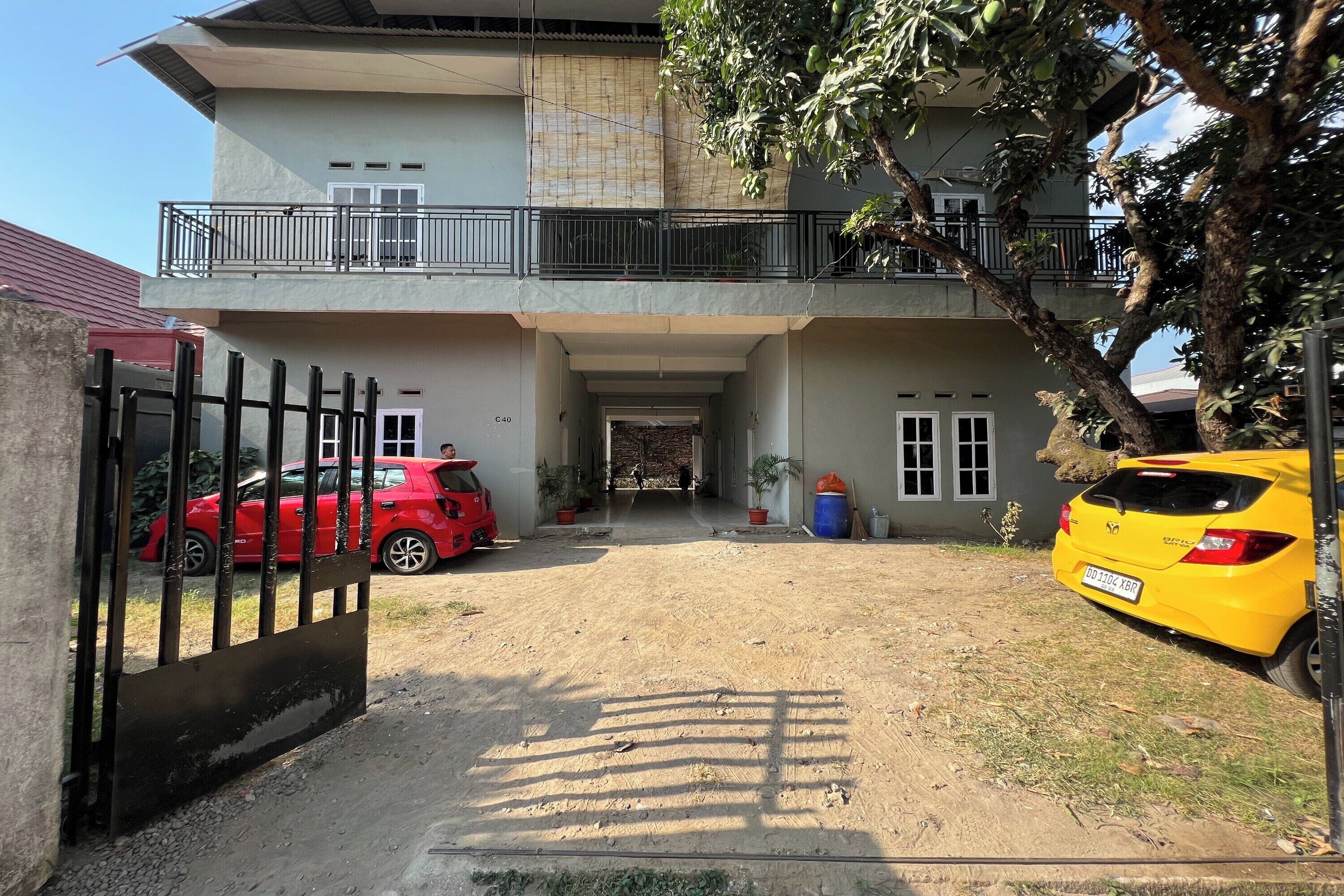 A two-story building with a gated entrance, a balcony, and two parked cars.