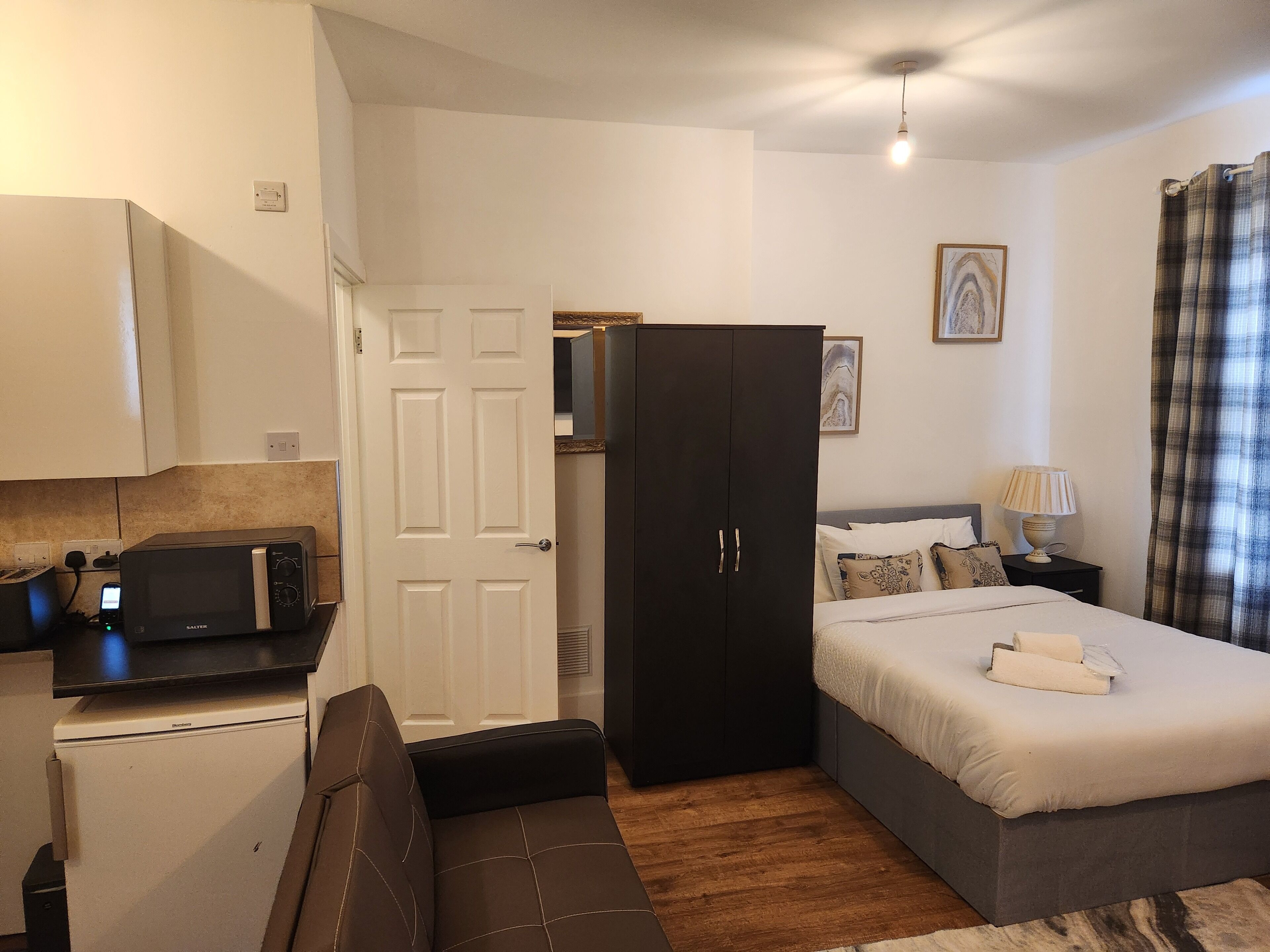 A compact bedroom with a bed, a wardrobe, a small kitchenette, and a sofa.