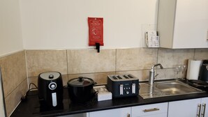 A kitchen with a coffee maker, toaster, and kettle on the counter, a sink, and a fire safety sign on the wall. - 1 Bed Flat - Sleeps 3 - Parking - Wifi (Greenhithe)