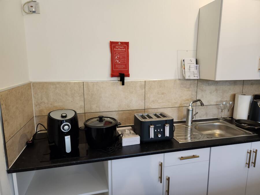 Una cocina con cafetera, tostadora y hervidor sobre la encimera, un lavabo y un letrero de seguridad contra incendios en la pared.