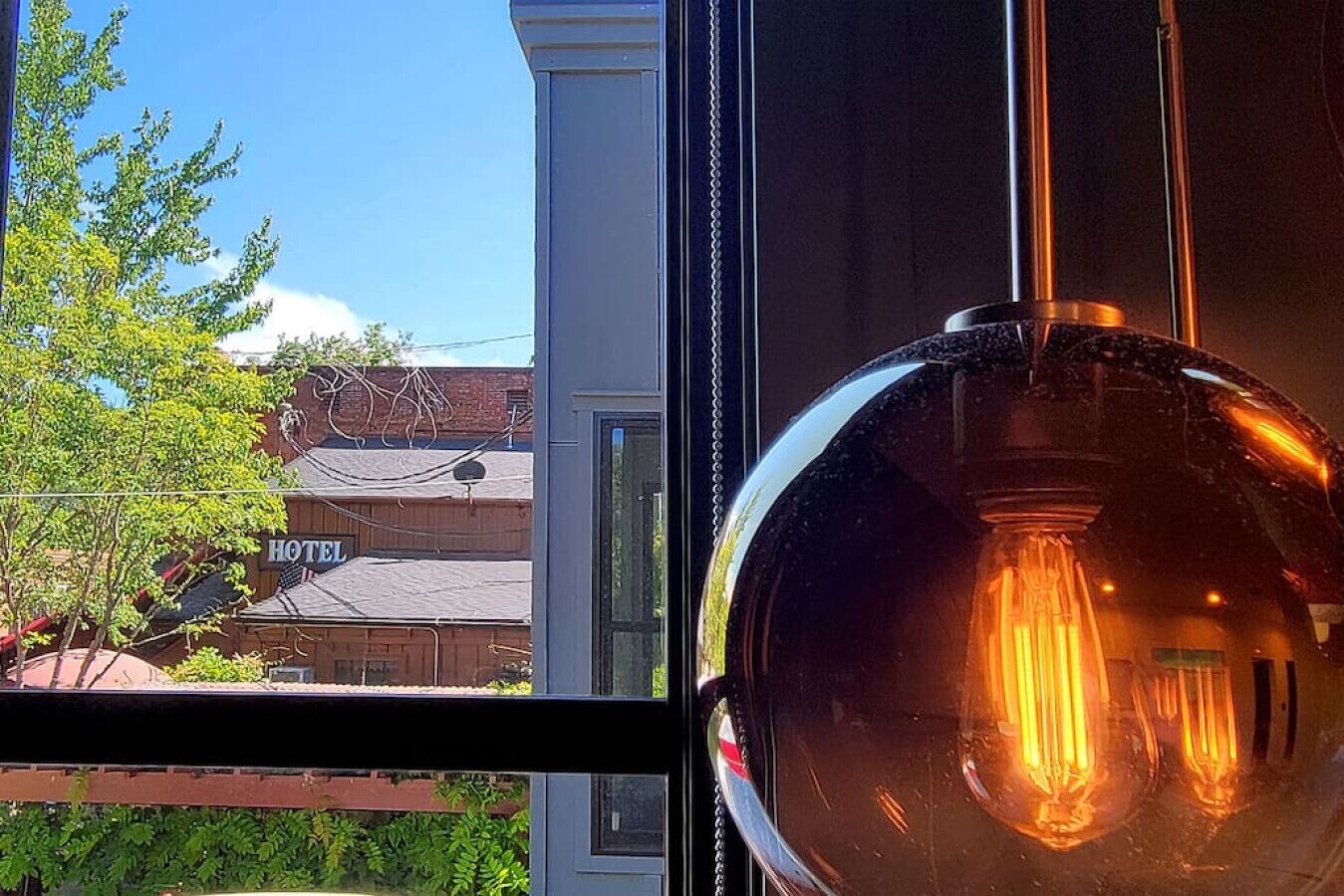 A view through a window with a hanging light bulb and a hotel sign in the background.