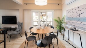 A modern living room with a round wooden table, black chairs, a grey armchair, a large TV, and a painting of birds. - Modern Apartment with Acropolis view (Athens)