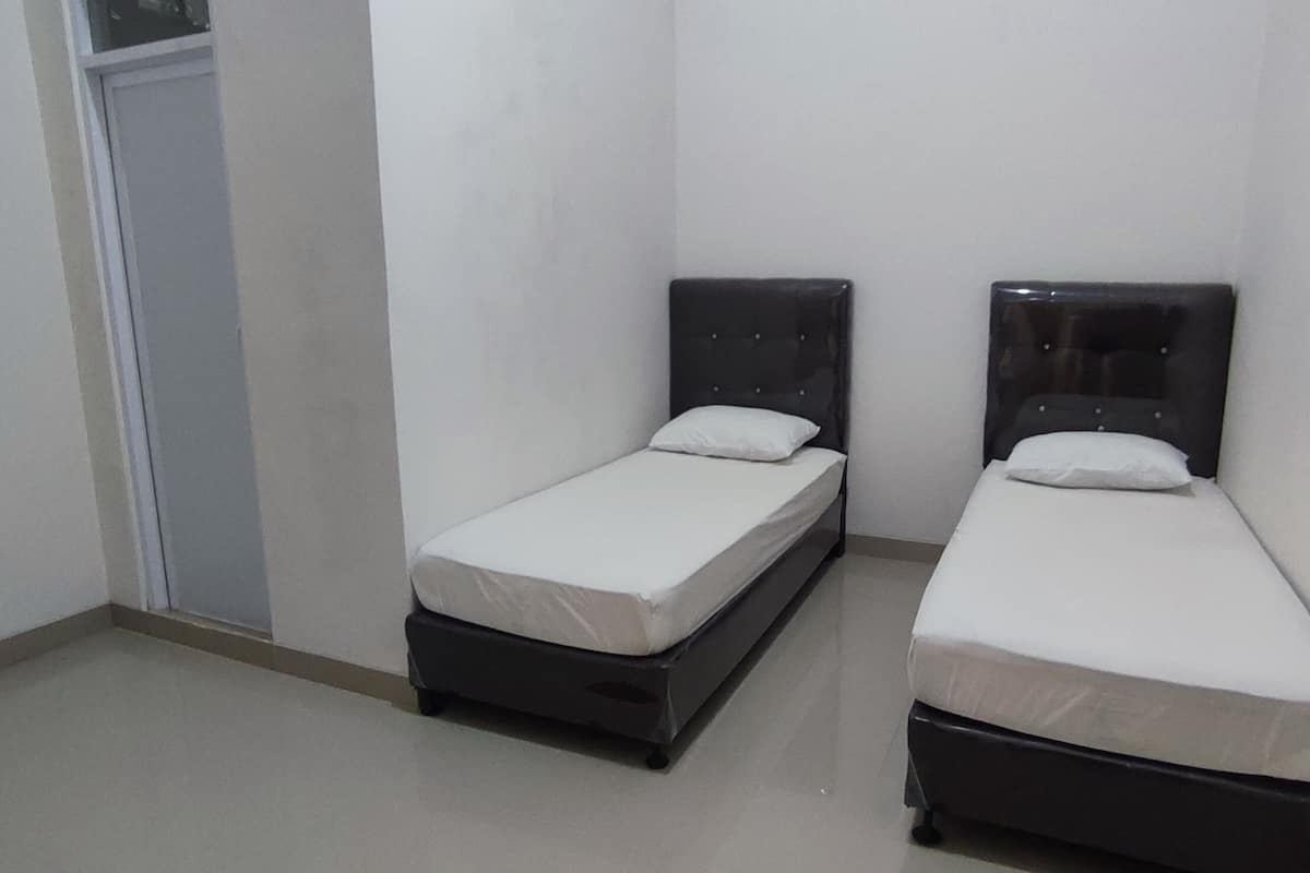A small, clean room with two single beds, a door, and a tiled floor.
