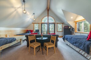A loft bedroom with a sloped ceiling, a loft bed, a desk with two chairs, a small table, and a large window with a view of trees. - Ember Ridge - Lake View w Guest Unit, Hot Tub, Ping Pong, Dog OK (Carnelian Bay)