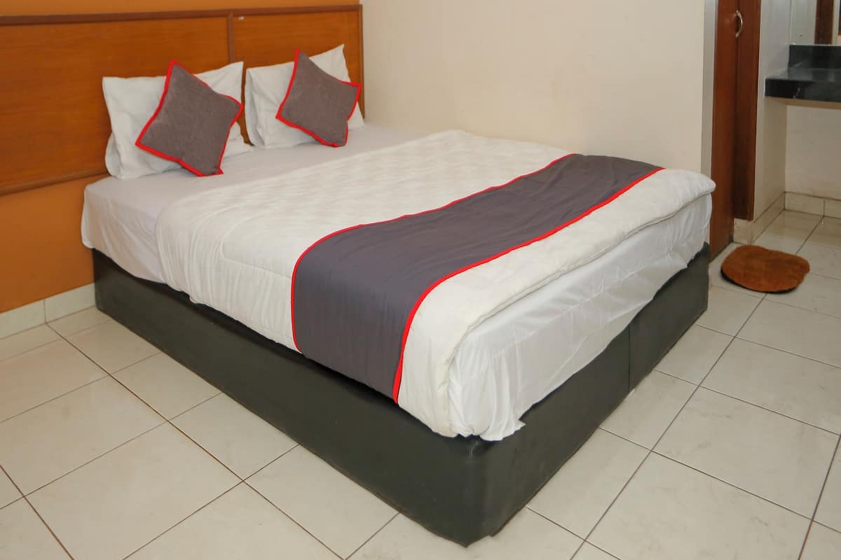 A neatly made bed with a white and gray bedspread, a wooden headboard, and a brown rug on the floor.
