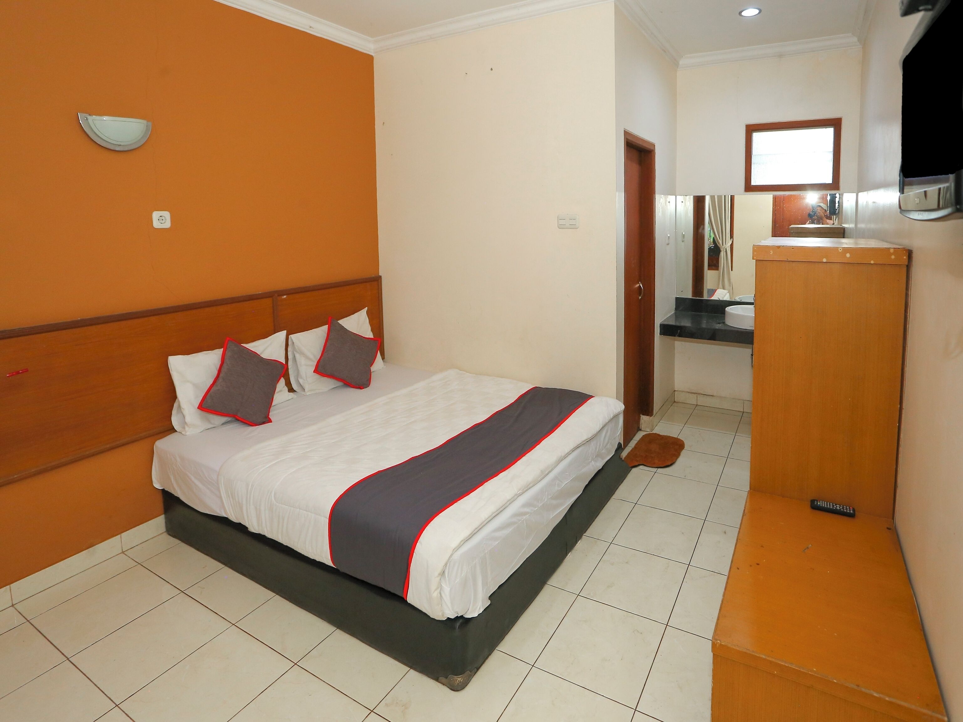 A hotel room with a bed, a wooden headboard, a small bathroom with a mirror, and a wooden cabinet.