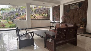 Une pièce spacieuse avec une grande fenêtre donnant sur un jardin. On y trouve un banc en bois et une petite table avec des chaises.