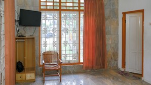 Une pièce comprenant une chaise en bois, un téléviseur fixé au mur, une armoire et une fenêtre avec un rideau.