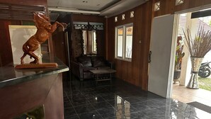 Un espace d’accueil doté d’un sol carrelé noir poli, d’un comptoir de réception en bois, d’un canapé en cuir et d’une statue équestre décorative.